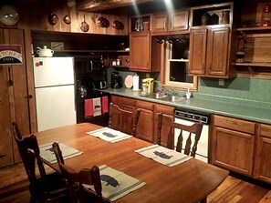 A kitchen with wooden cabinets, a refrigerator, a sink, and a dining table with chairs. - Cozy Vacation Rental with High-Speed Wi-Fi near Seven Springs, Pennsylvania (Champion)