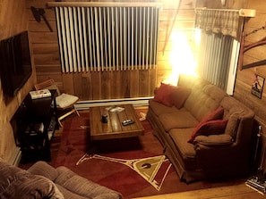A cozy living room with a wooden wall, a sofa, a coffee table, and a television. - Cozy Vacation Rental with High-Speed Wi-Fi near Seven Springs, Pennsylvania (Champion)