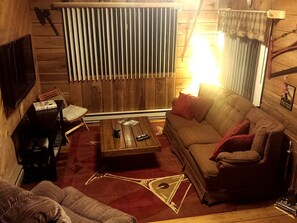 A cozy living room with a wooden wall, a sofa, a coffee table, and a television.