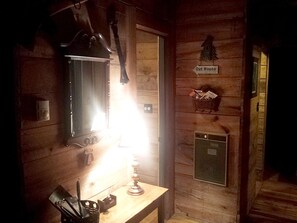 A wooden cabin interior with a desk, a lamp, a mirror, a small cabinet, and a sign reading 'Out House.'