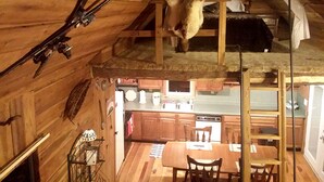 A rustic cabin interior with a dining area, kitchen, and a sleeping loft. - Cozy Vacation Rental with High-Speed Wi-Fi near Seven Springs, Pennsylvania (Champion)