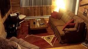 A cozy living room with a wooden wall, a sofa, a coffee table, and a television. - Cozy Vacation Rental with High-Speed Wi-Fi near Seven Springs, Pennsylvania (Champion)