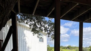 A covered outdoor area with a barbecue grill, wooden deck, and a white cabin-like structure. - Peaceful Texas Hill Country Rental Perfect for Glamping Around Austin (Dripping Springs)
