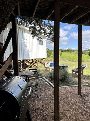 Ein überdachter Außenbereich mit Grill, Holzterrasse und einem weiß gestrichenen Häuschen.