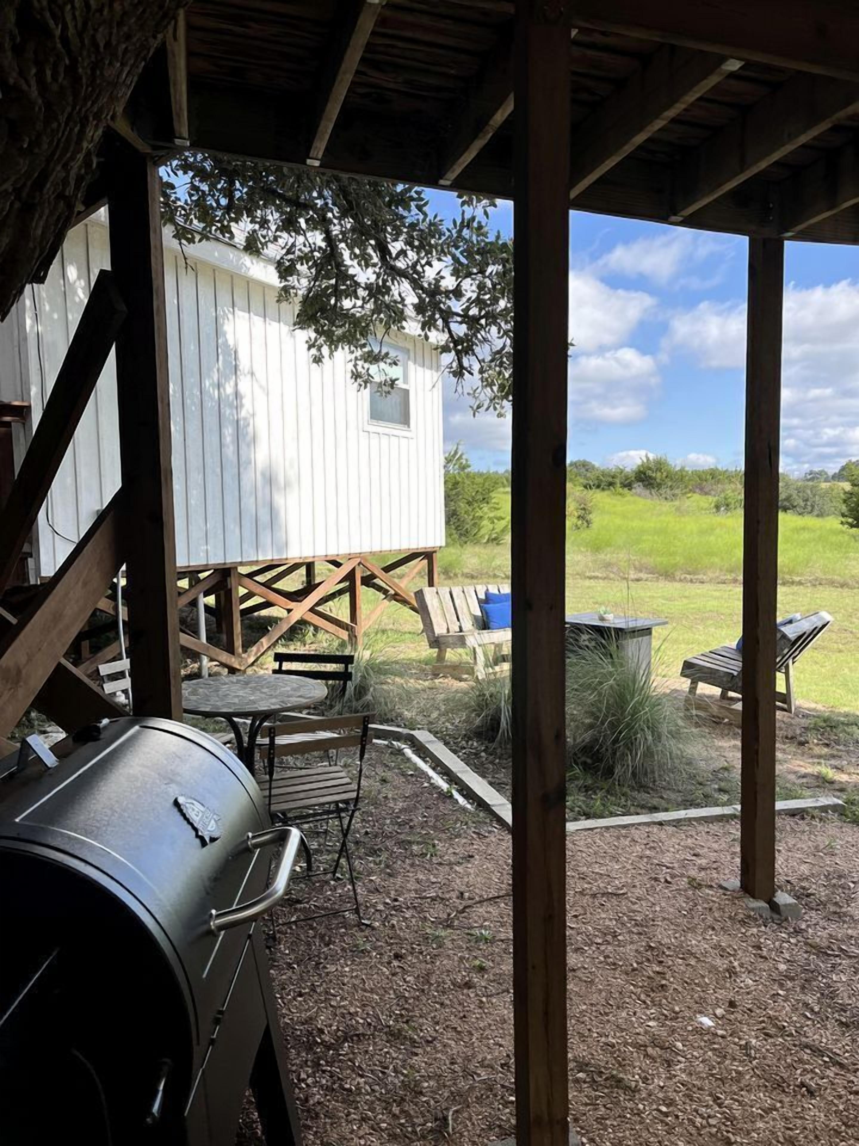 A covered outdoor area with a barbecue grill, wooden deck, and a white cabin-like structure.