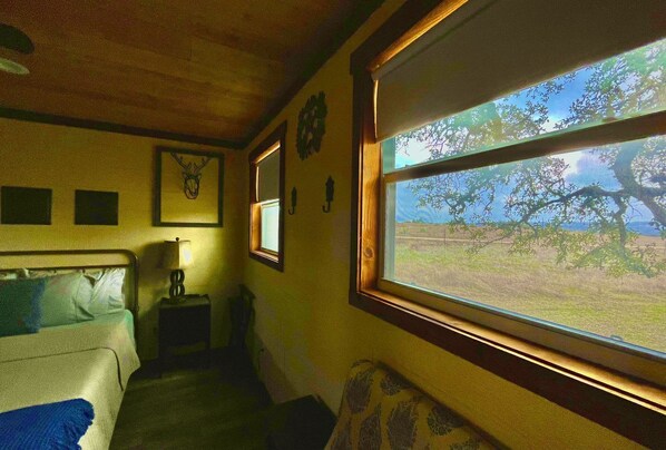 A room with a bed, a nightstand, a window with a view of trees, and a wall clock.