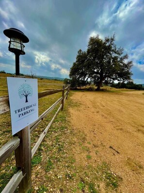A sign for treehouse parking, a wooden fence, a large tree, and a dirt path.