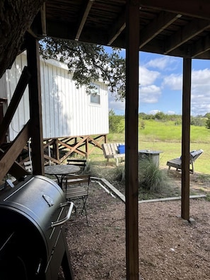 Een overdekt buitengebied met een barbecue, een houten terras en een witte, op een blokhut lijkende constructie.