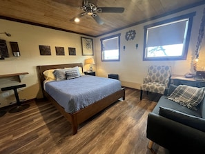 A bedroom with a bed, a chair, a desk, and a ceiling fan.