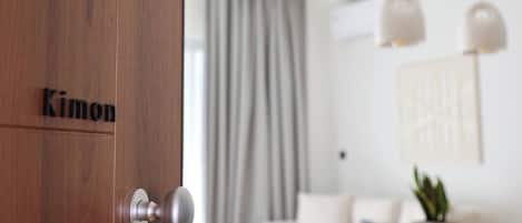 Un interior moderno con una puerta de madera que dice 'Kimon', un área de comedor con mesa y sillas, y un espacio de sala con sofá y una planta.