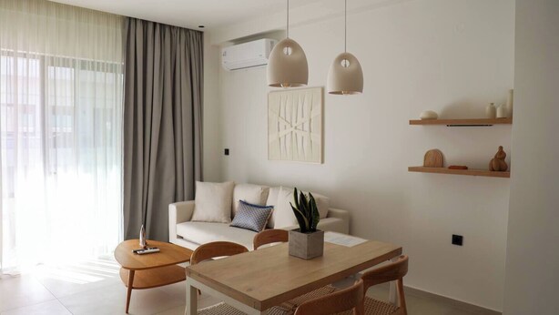 Ein modernes Wohnzimmer mit Sofa, Esstisch, Stühlen, Pendelleuchten und einer Zimmerpflanze.