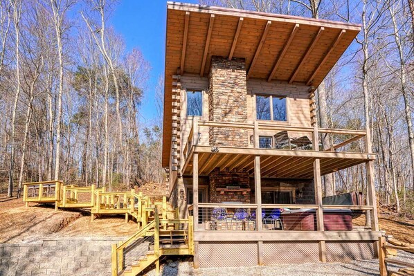 A multi-story log cabin with a stone chimney, wooden deck, and a staircase leading to the entrance.
