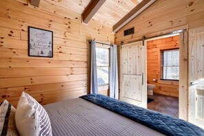 Habitación de cabaña de madera con una cama, una cita enmarcada en la pared y una puerta que da a un baño.