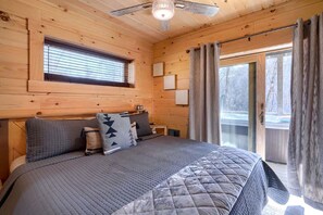A wooden cabin bedroom with a bed, pillows, a window, and a door leading to a balcony. - Restful Getaways to Logan, Ohio, in this Fully-Equipped Log Cabin with Fireplace and Hot Tub (Logan)