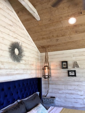 Une pièce avec un plafond en bois, une tête de lit capitonnée, une lanterne suspendue et une couronne décorative accrochée au mur.