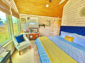 Een slaapkamer met een bed, een stoel, een bureau en een raam.