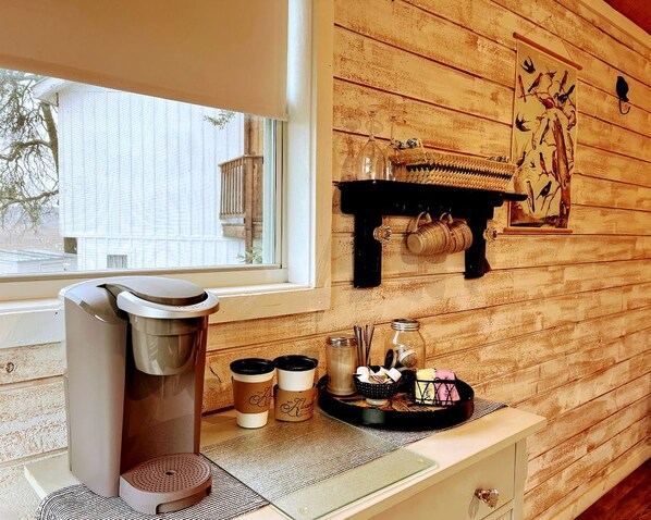 A room with a coffee machine, a tray with coffee cups, a basket, and a wall-mounted shelf with decorative items.