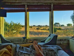 Een kamer met een bed, twee stoelen en een raam met uitzicht over een veld.