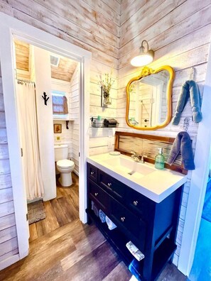 Een badkamer met een houten vloer, een wit wastafelmeubel met spiegel en een toilet.