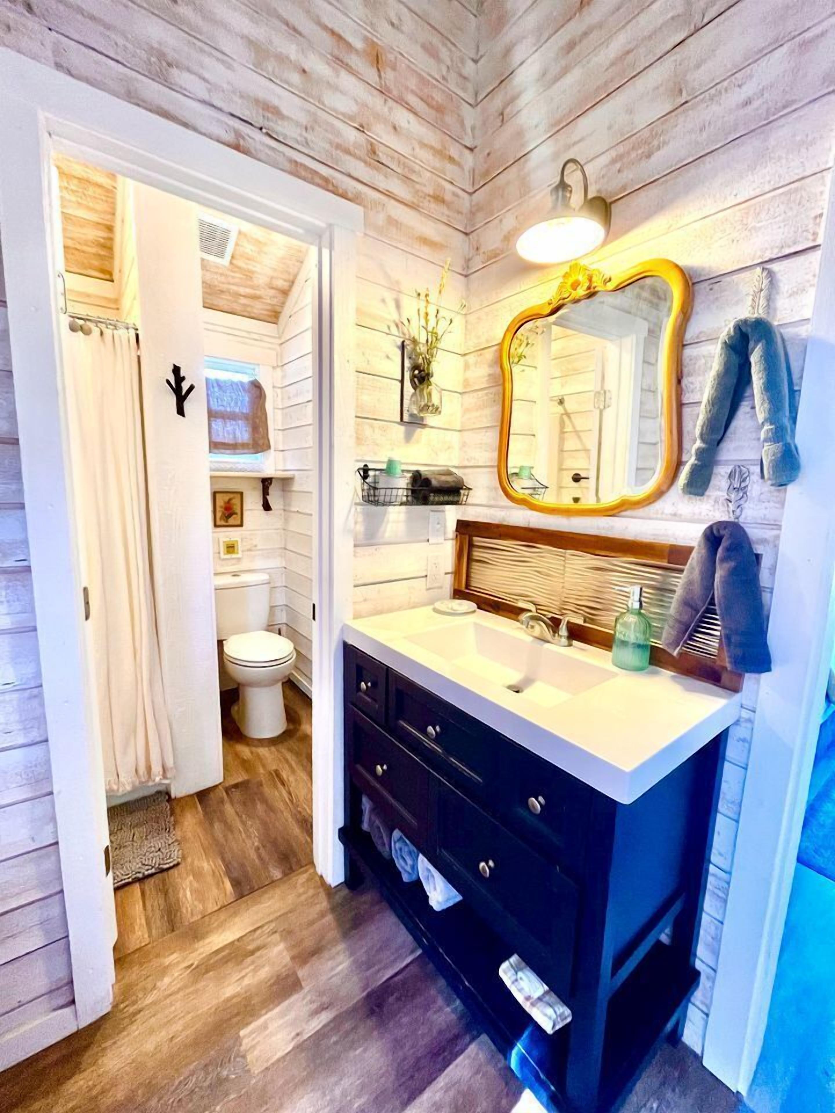 A bathroom with a wooden floor, a white sink with a mirror, and a toilet.