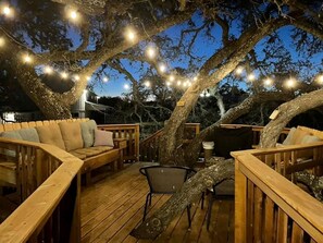 An outdoor deck with wooden furniture, string lights, and a large tree.