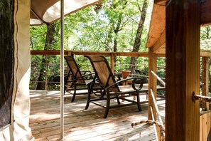 Een houten terras met stoelen en een tafel, omringd door bomen.