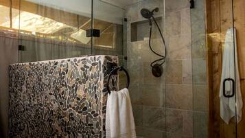 A shower with a stone mosaic wall, a towel rack, and a wooden door.