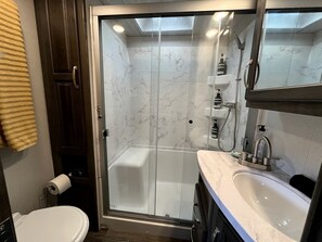 A modern bathroom with a glass-enclosed shower, a white sink, and a toilet.