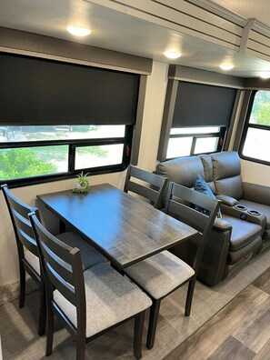 A compact RV interior with a dining table, chairs, a sofa, and a small potted plant.