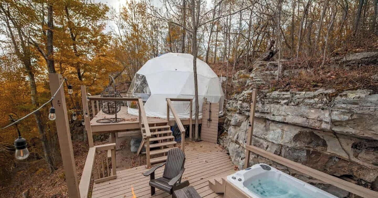 Uma tenda com deck de madeira, hidromassagem e uma cadeira.
