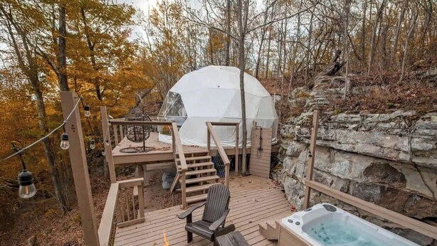 A wooden deck with a hot tub, a chair, and a tent in a forested area.