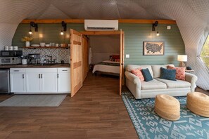 Un espacio habitable pequeño con kitchenette, un conjunto de sofá y un tapete estampado.