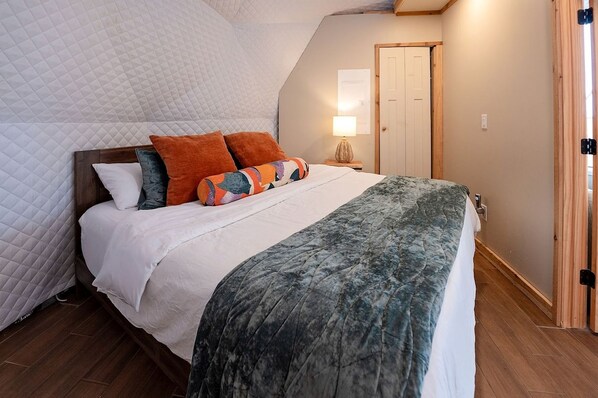 Un dormitorio con cama, almohadas, una lámpara de noche y una puerta.