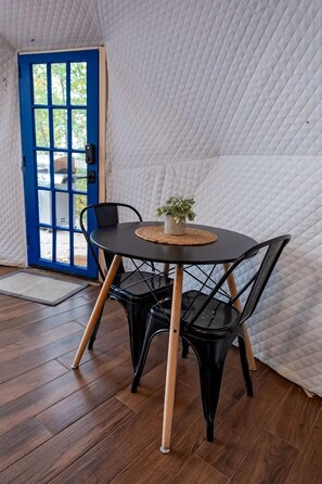 A room with a round table, black chairs, a blue door, and a white quilted wall. - Off-Grid Dome with Private Hot-Tub and Spectacular Sunrise Views in Tennessee (Altamont)