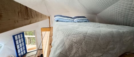 Un dormitorio con cama, almohadas, una ventana y vistas al exterior.
