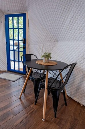 Een kamer met een ronde tafel, zwarte stoelen, een blauwe deur en een gewatteerde witte muur.