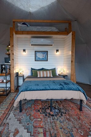 Een slaapkamer met een stapelbed, een groot vloerkleed, een kaart aan de muur en een klein plankje met spullen.