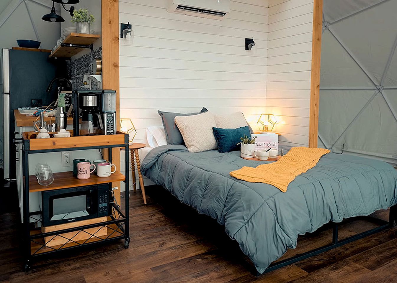 Una habitación compacta con cama, mesita de noche y un escritorio pequeño con cafetera.