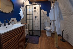 Een moderne badkamer met een houten wastafelmeubel, een douchecabine van glas, een toilet en een wand betegeld met blauw-wit zeshoekige tegels.