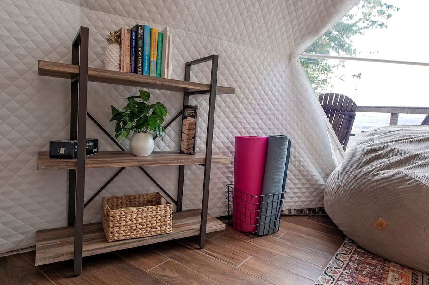 A room with a quilted wall, a wooden bookshelf, a potted plant, rolled yoga mats, and a bean bag.