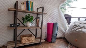 A room with a quilted wall, a wooden bookshelf, a potted plant, rolled yoga mats, and a bean bag.
