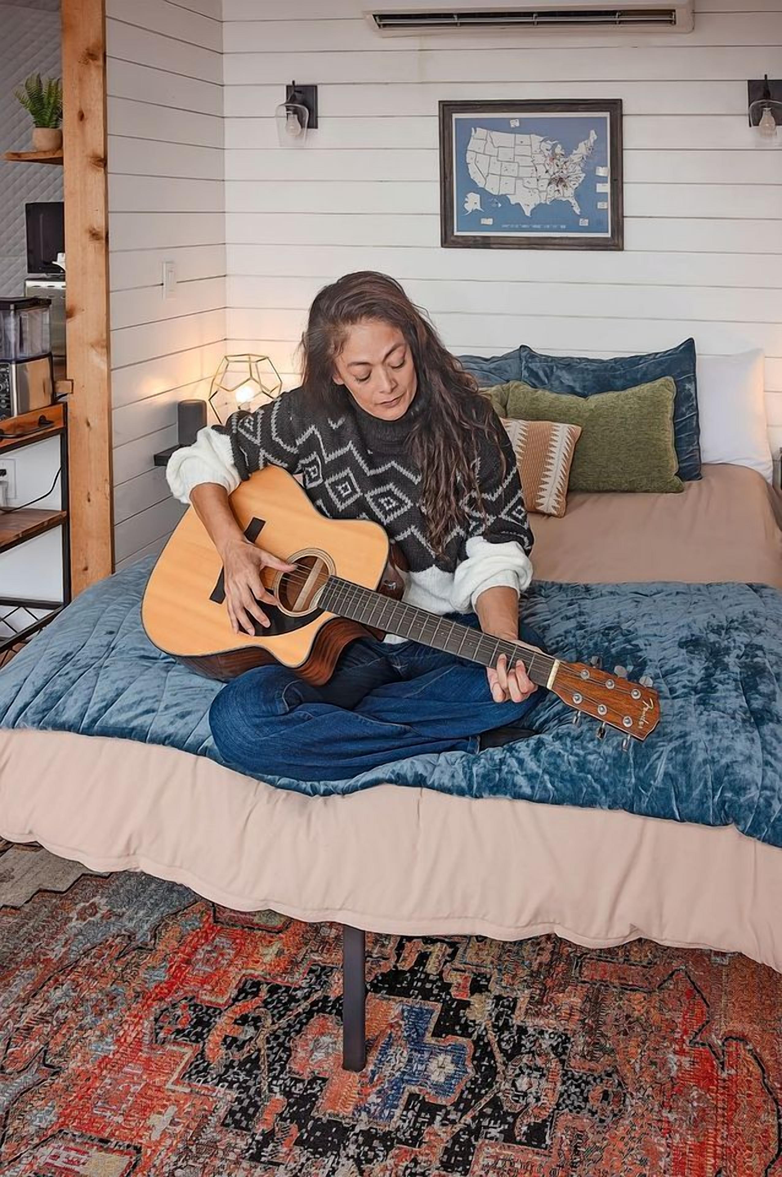 Una persona seduta su un letto che suona la chitarra.