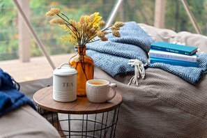 Een gezellig hoekje om te lezen, met een klein tafeltje, een vaas met gedroogde bloemen, een theepot, een kopje en een stapel boeken.