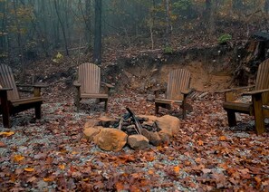 Un décor forestier avec un foyer et quatre chaises Adirondack.