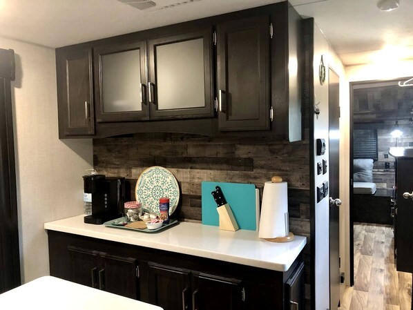 A kitchen with dark cabinets, a white countertop, a coffee maker, a knife block, and a plate with a floral design.