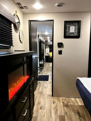 A compact RV interior with a kitchenette, a bed, and a door leading to a dining area.