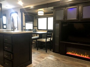 A kitchen with a dining area, a large flat-screen TV, and a fireplace.