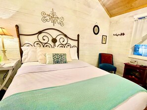 Ein Bett mit Kopfteil, Kissen, Decke, ein Stuhl, ein Nachttisch, eine Wanduhr und ein Fenster.