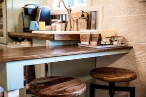 A kitchen counter with a coffee machine, a sink, and two stools.