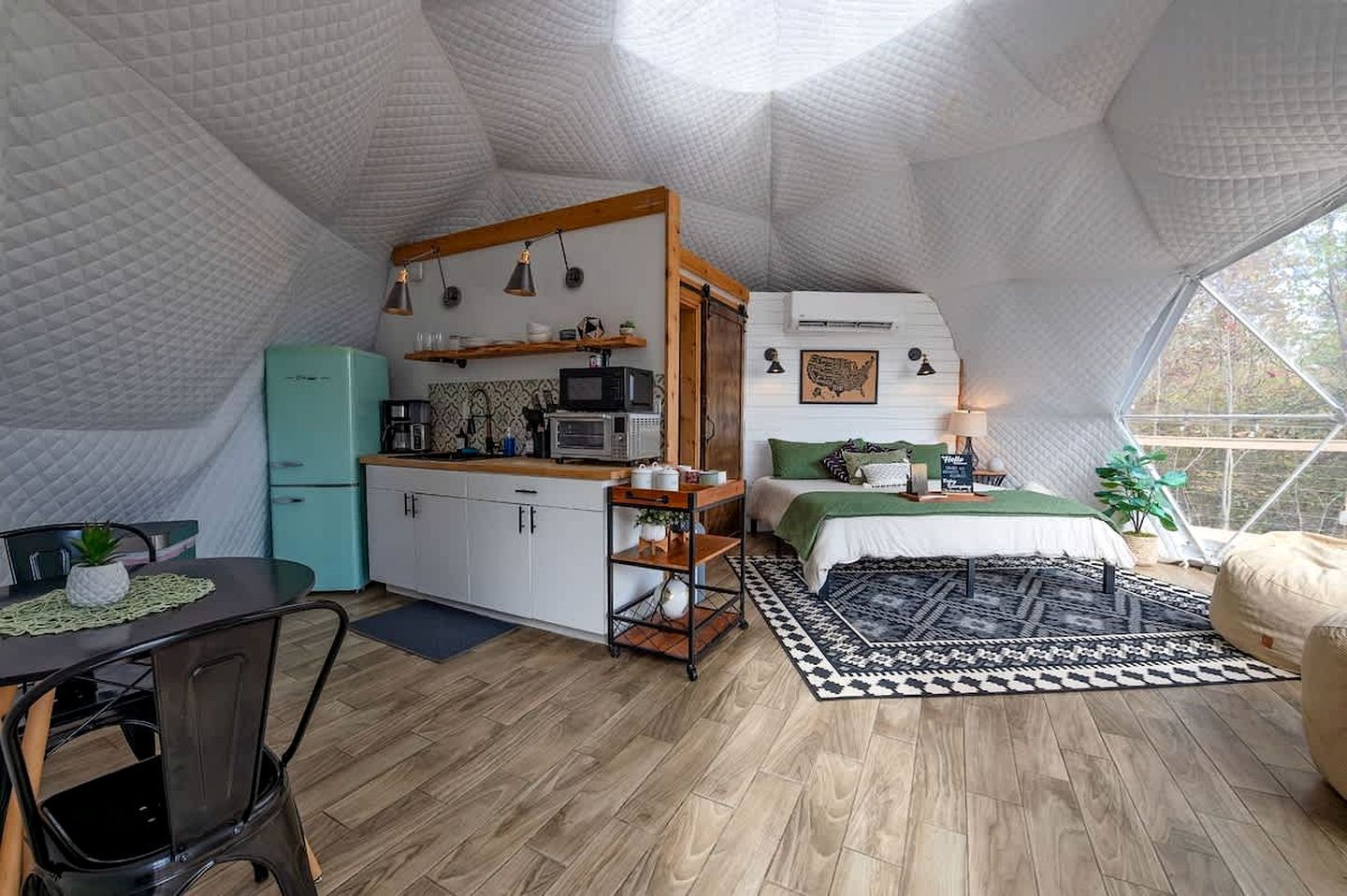 A compact, tent-like interior with a kitchenette, a bed with green bedding, and a dining area with a table and chairs.